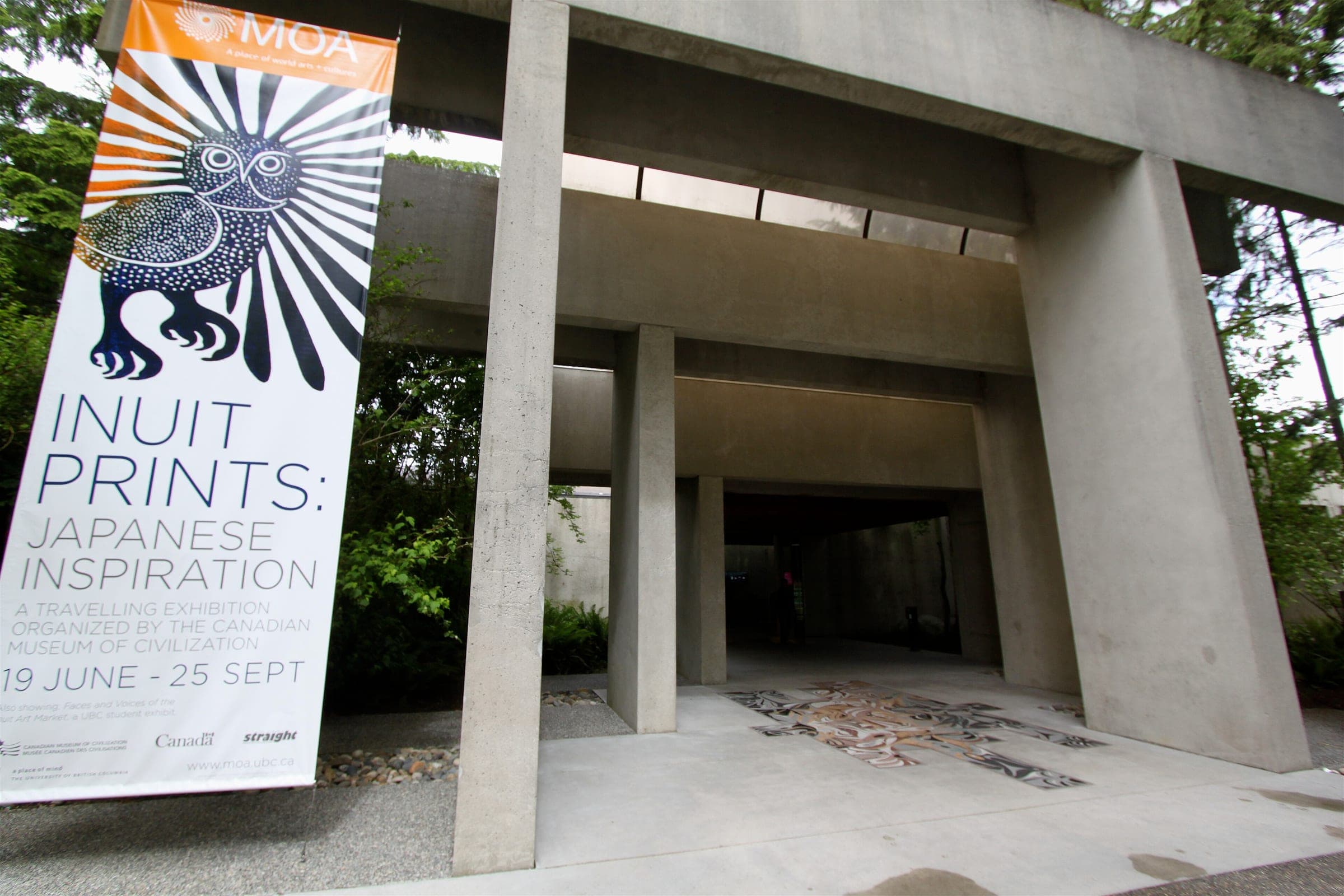 Concrete entrance to the Museum of Anthropology at UBC with an exhibition banner beside the doors.