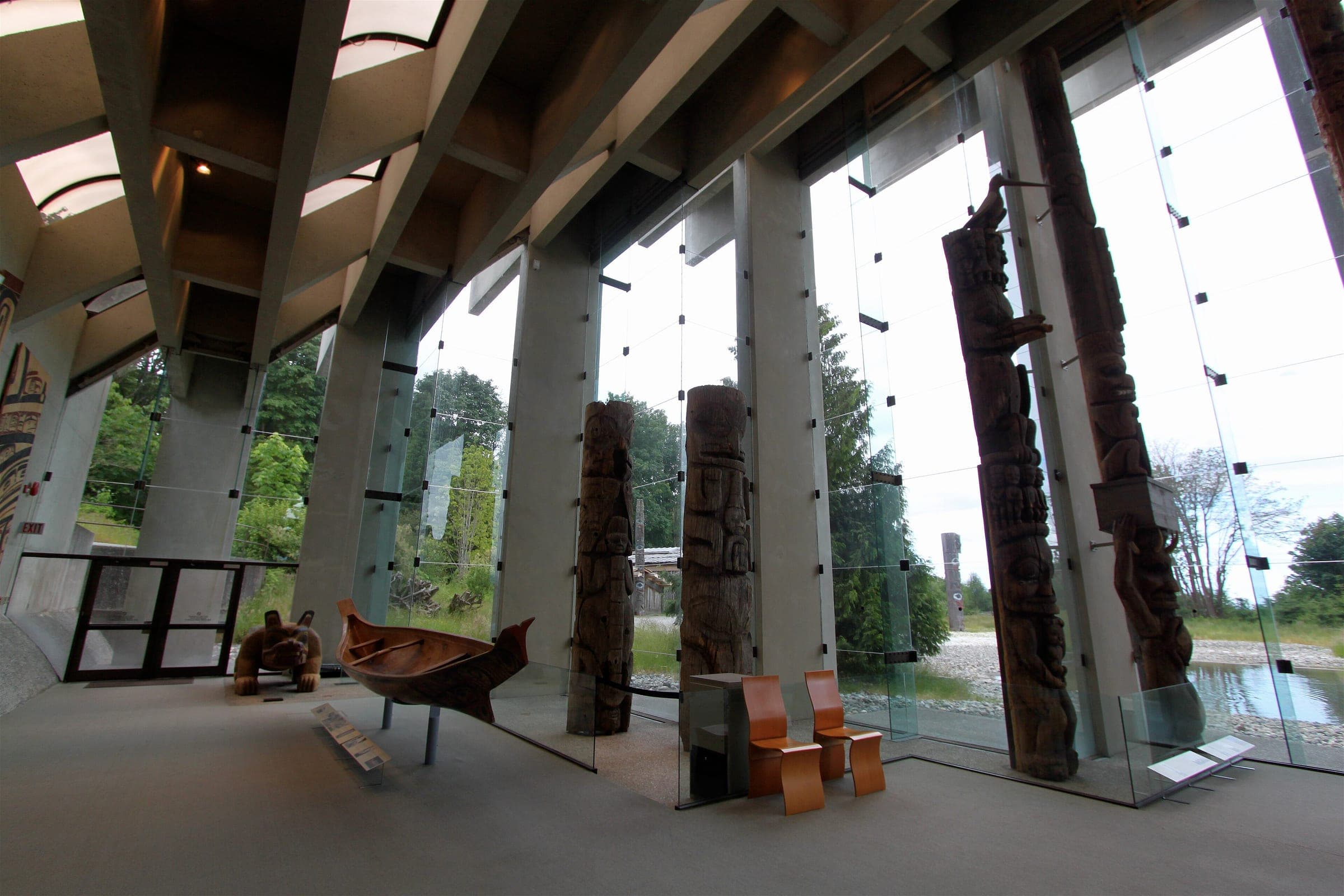Main hall of the Museum of Anthropology at UBC with tall carved poles standing against the glass wall.