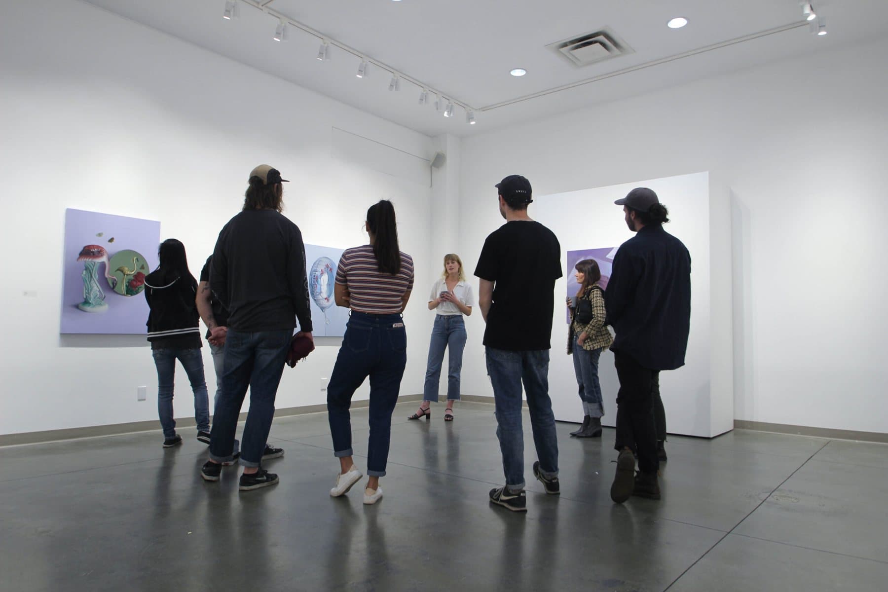 Visitors standing in a white-walled room at the Seymour Art Gallery looking at paintings.