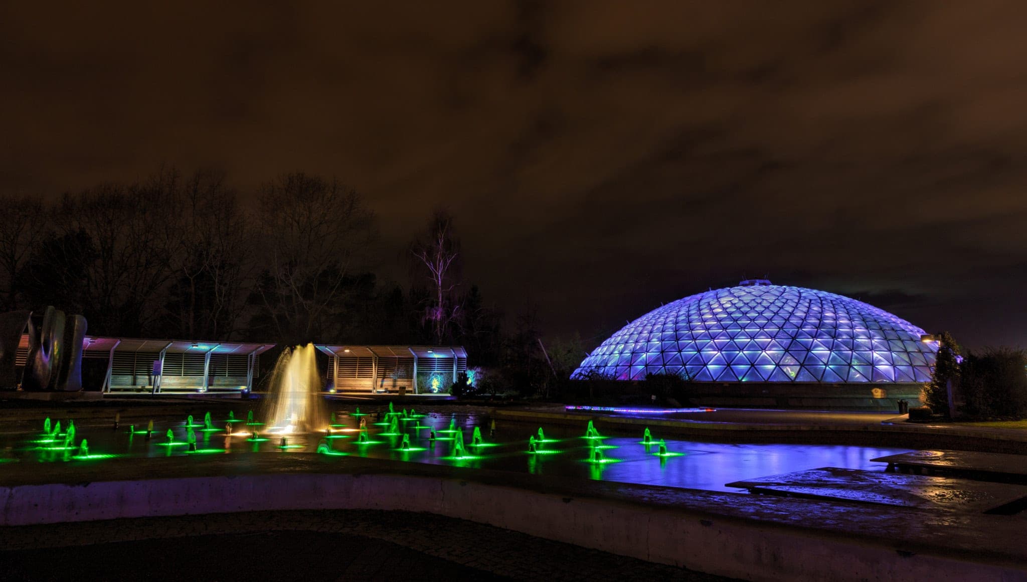 The Bloedel Conservatory dome glows blue at night above the lit fountains of Queen Elizabeth Park.
