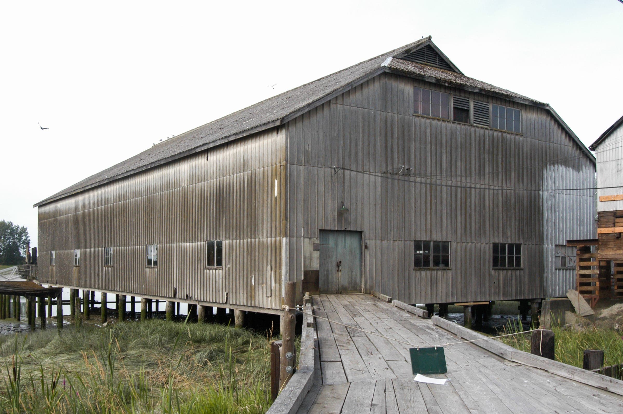 A boardwalk leads to a grey timber shed raised on pilings at Britannia Heritage Shipyards.