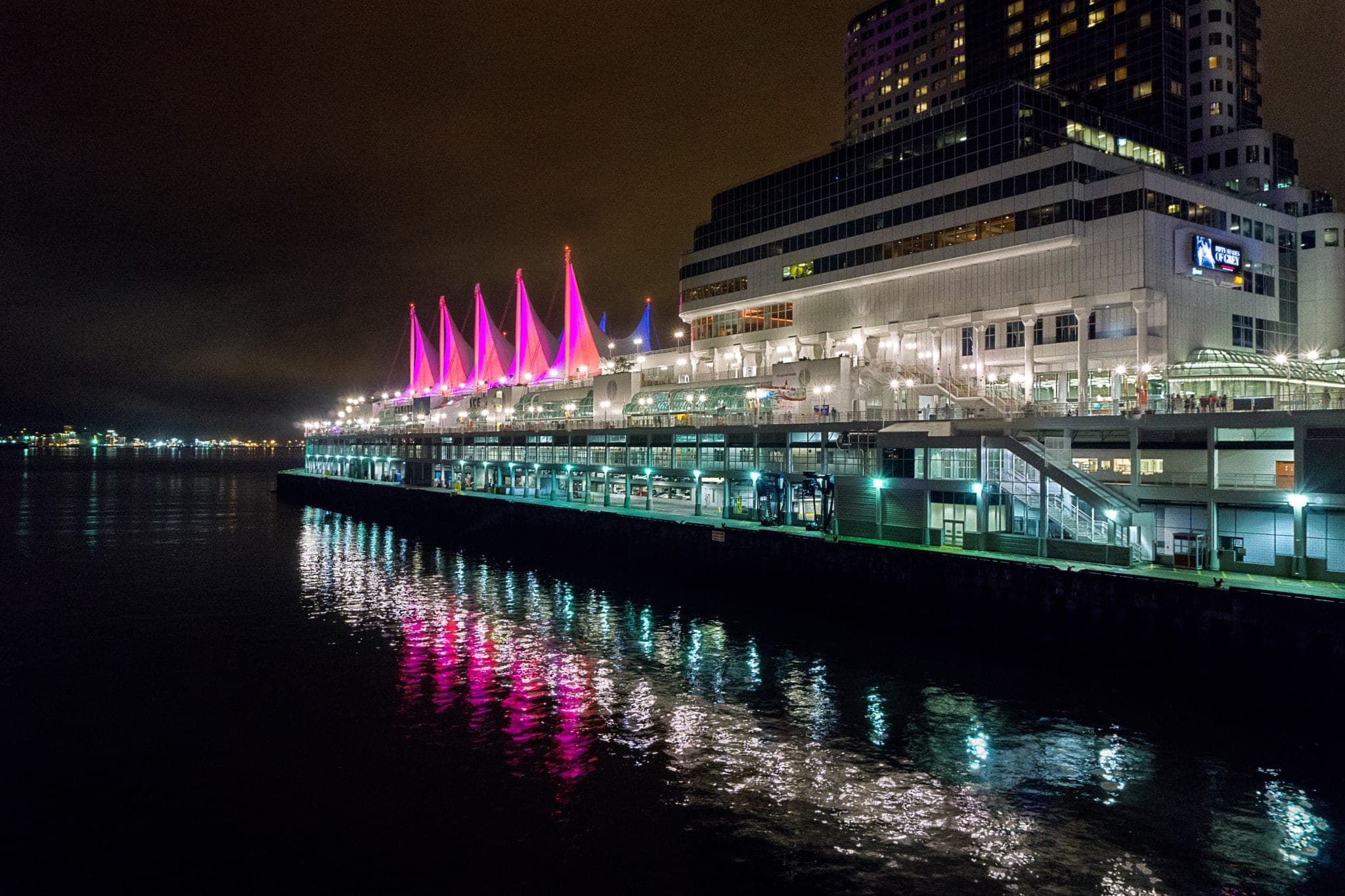 Canada Place's sails glow pink at night and throw their colour across the dark harbour.