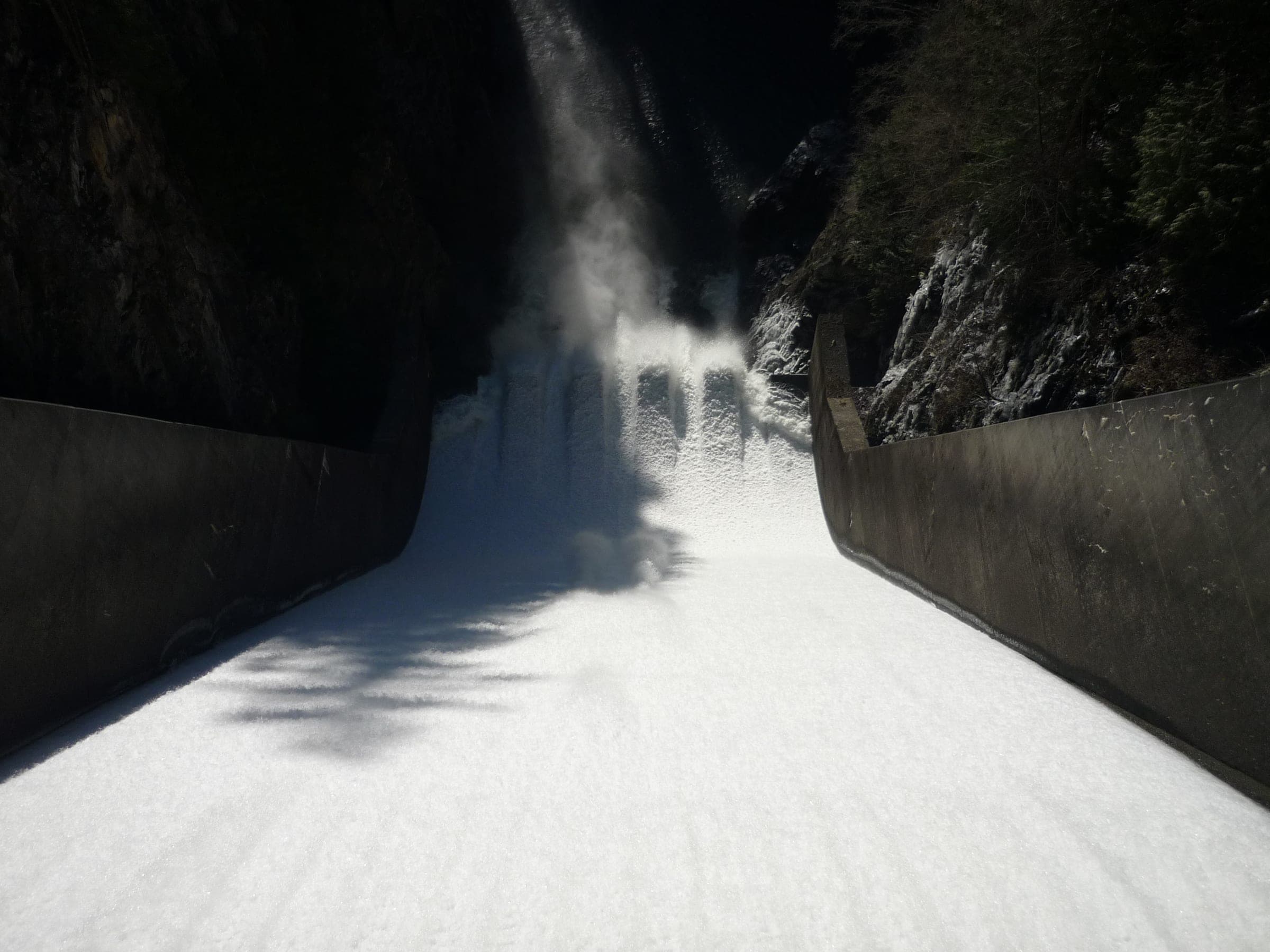Water thunders down the spillway of Cleveland Dam into the Capilano canyon in winter sun.