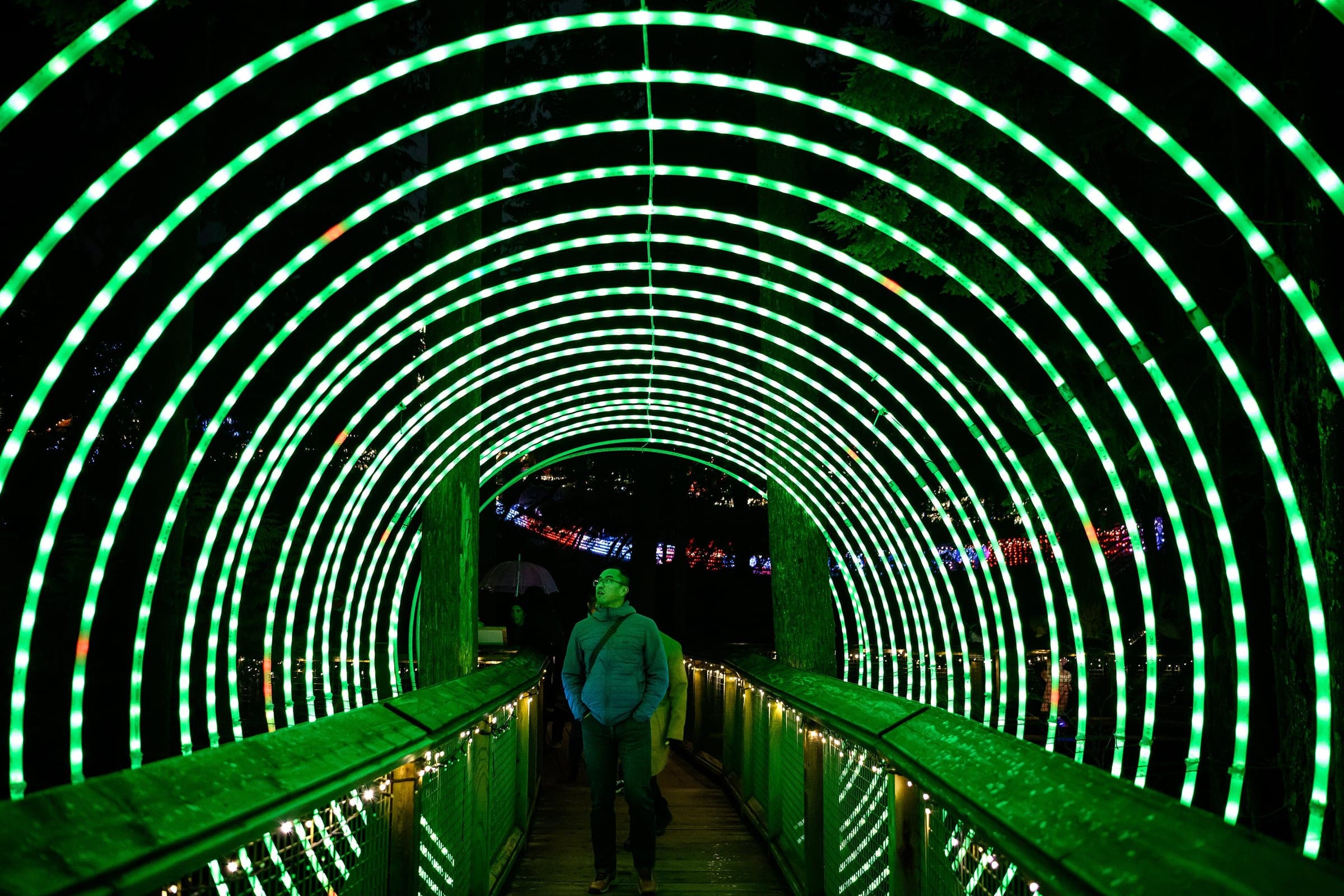 Green light hoops arch over a walkway at Capilano Suspension Bridge Park during Canyon Lights.