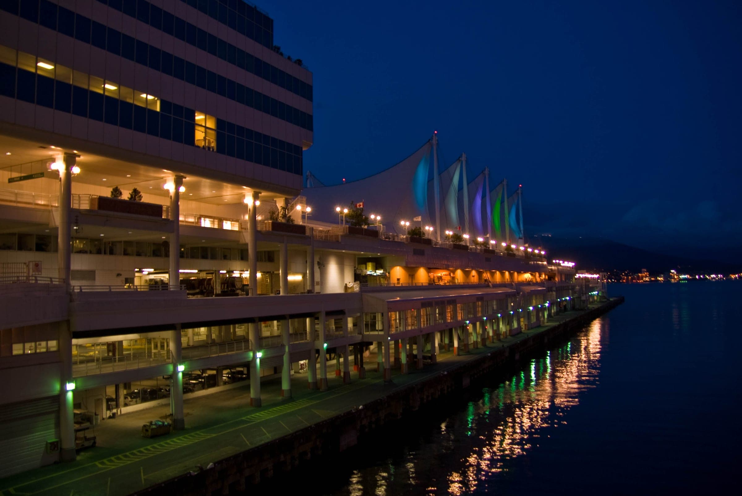Lamps light the promenade of Canada Place at night where FlyOver Canada sits under the sails.