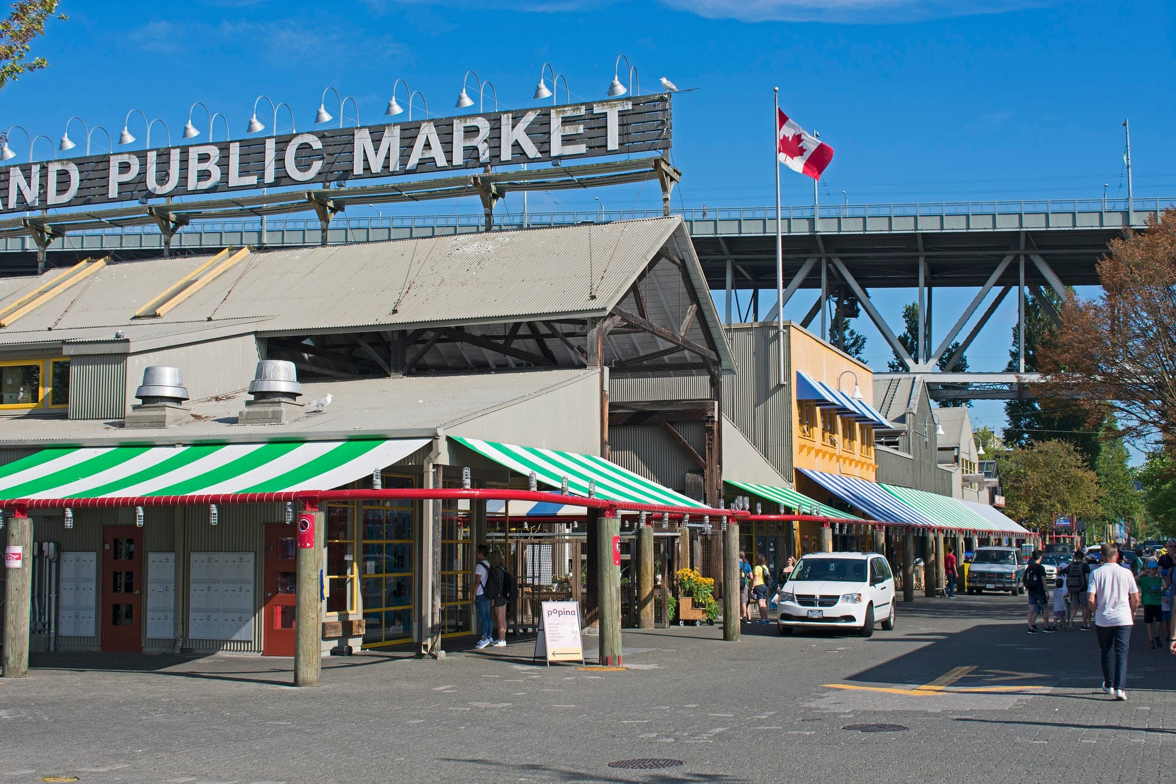 Striped awnings line the Granville Island Public Market under its rooftop sign and the Granville Bridge.