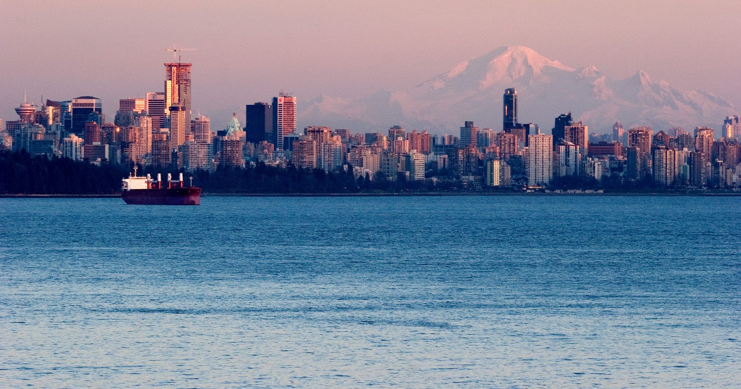 Downtown Vancouver and snowy Mount Baker glow pink at dusk across the water from Lighthouse Park.