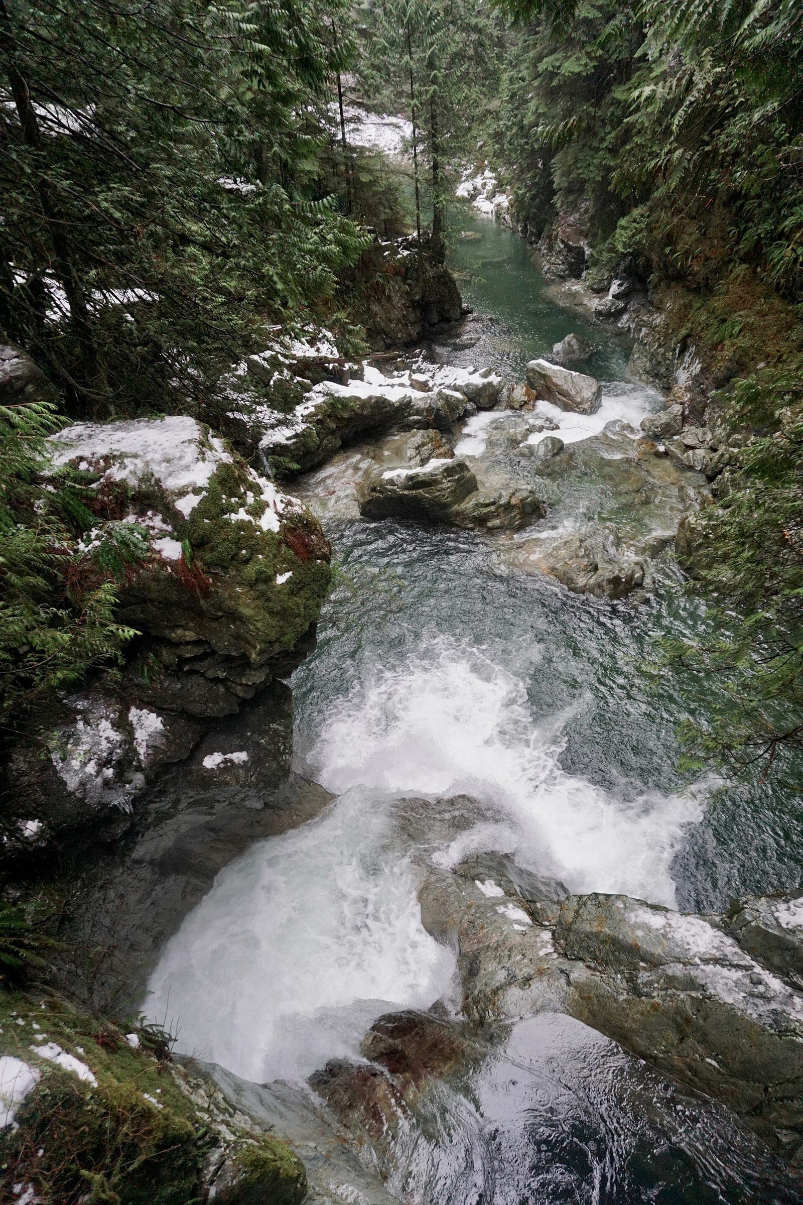 Snow lines the granite as Lynn Creek pours into green pools below the canyon in Lynn Canyon Park.