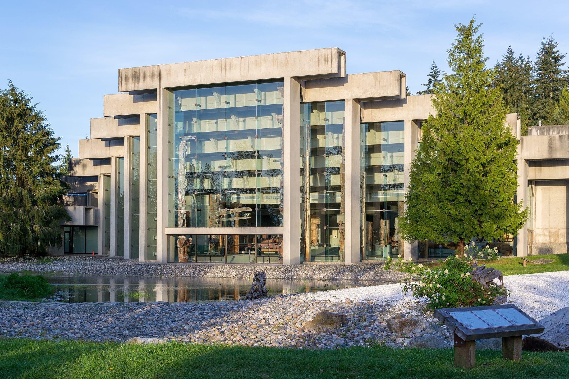 The glass and concrete Great Hall of the Museum of Anthropology at UBC rises behind its pond.