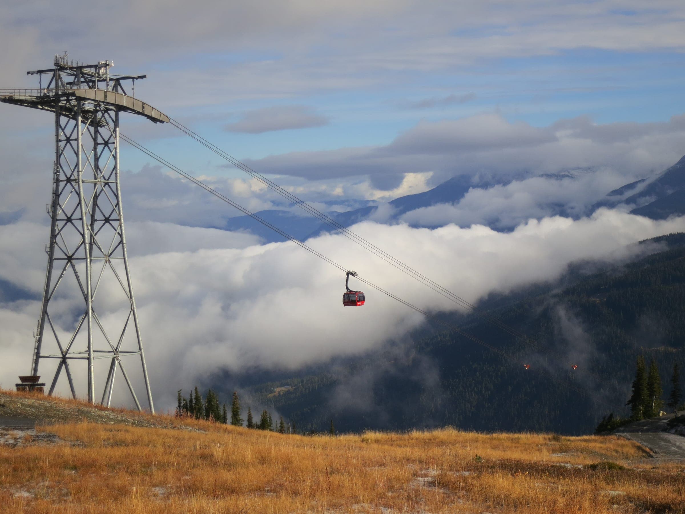 A Peak 2 Peak tower carries a cabin over a sea of cloud above golden autumn meadow on Whistler.