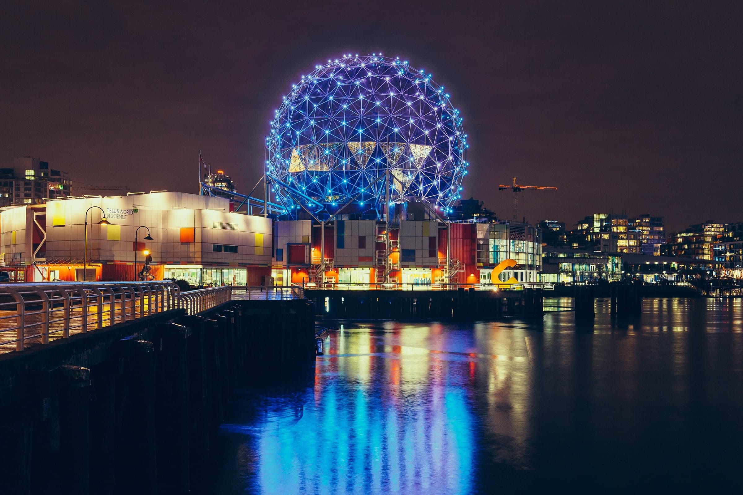 Science World's geodesic dome glows blue over the still water of False Creek on a December night.