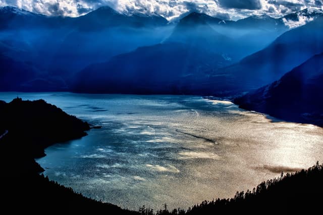 Sun glints on Howe Sound below blue ridges in the view from the summit of the Sea to Sky Gondola.