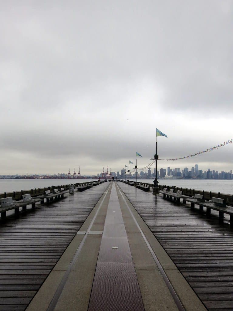 Burrard Dry Dock Pier runs out from the Shipyards toward the downtown Vancouver skyline on a grey day.