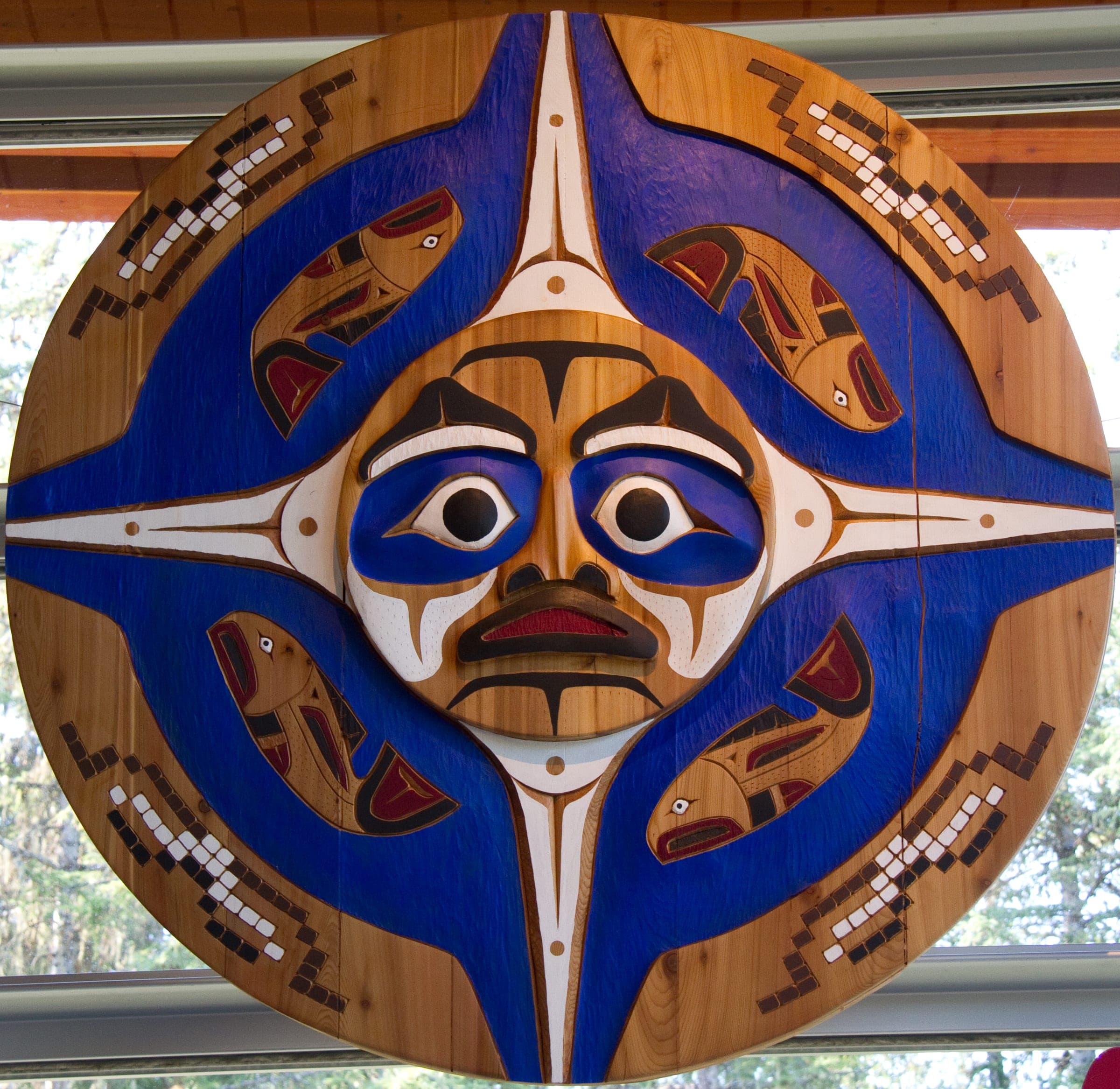 A painted wall disc with a face and fish designs inside the Squamish Lil'wat Cultural Centre.