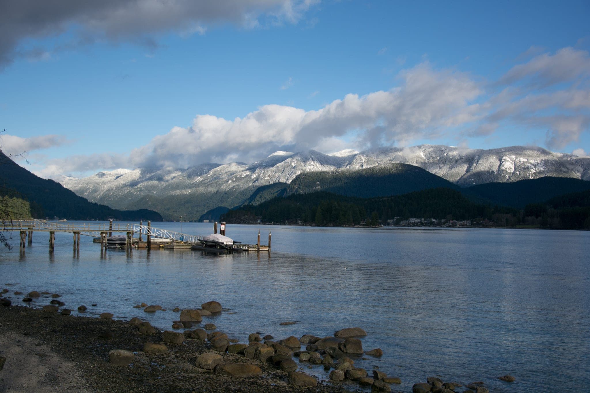 Snow-capped peaks rise above Indian Arm seen from the rocky shore of Whey-ah-Wichen/Cates Park.