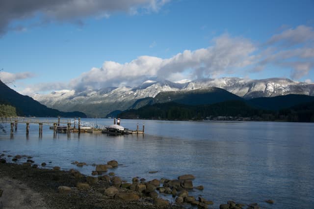 Snow-capped peaks rise above Indian Arm seen from the rocky shore of Whey-ah-Wichen/Cates Park.