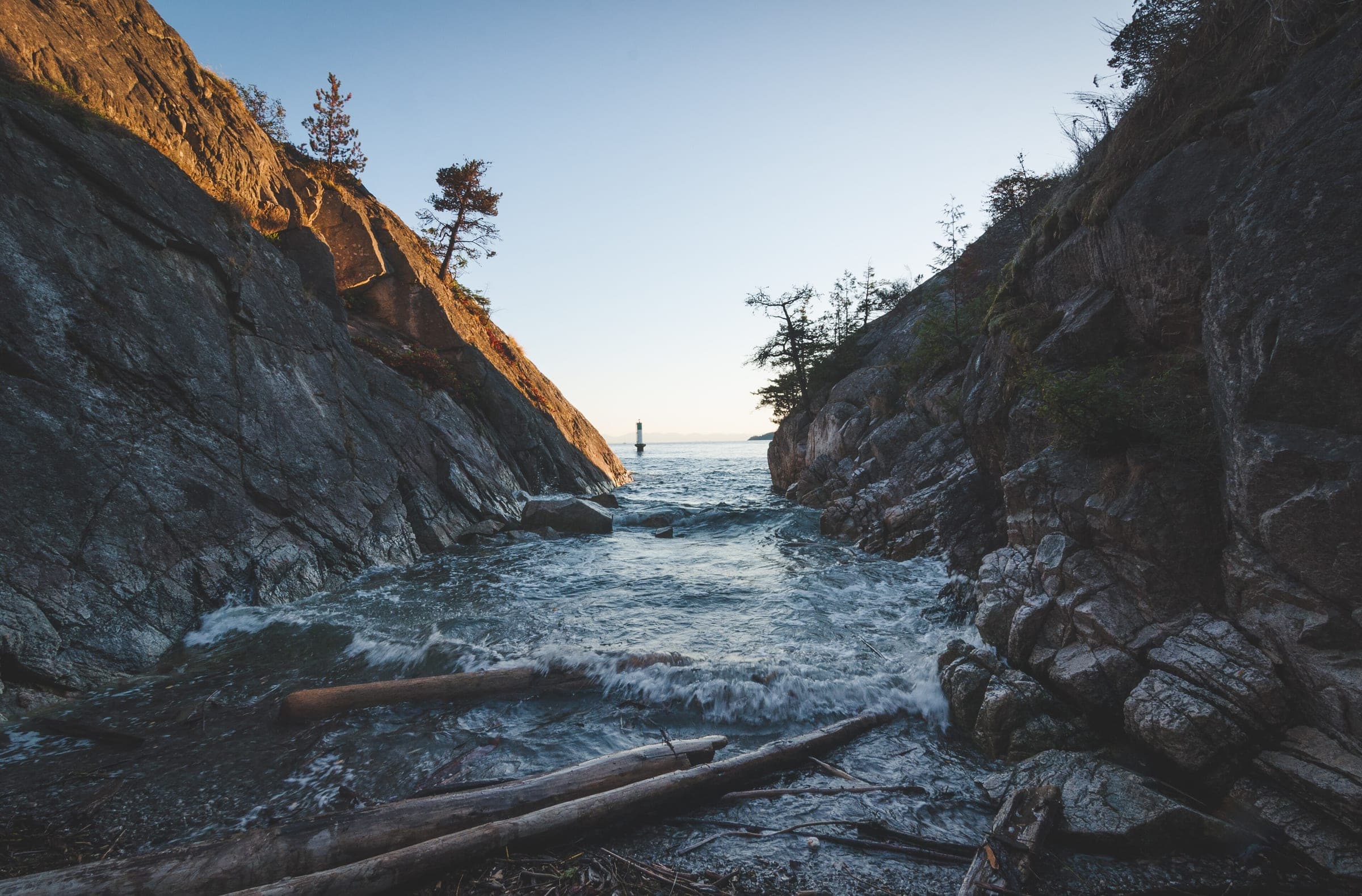 Waves surge between granite cliffs into a driftwood cove at Whytecliff Park at dusk.
