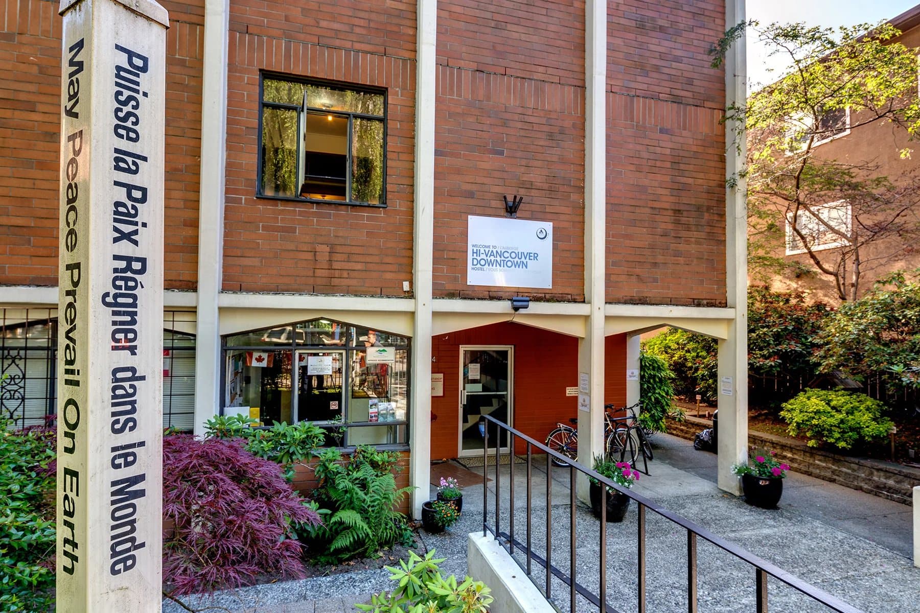 Brick entrance and garden frontage of HI Vancouver Downtown hostel with its peace pole.