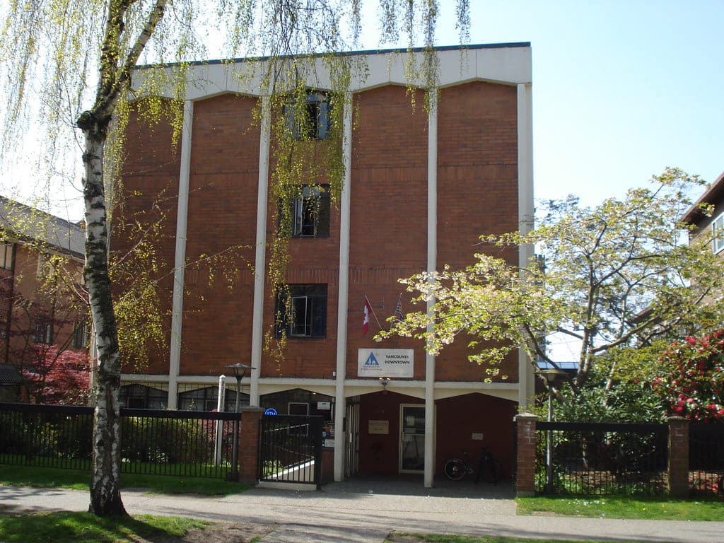 Brick front of HI Vancouver Downtown on Burnaby Street with flowering trees in spring.