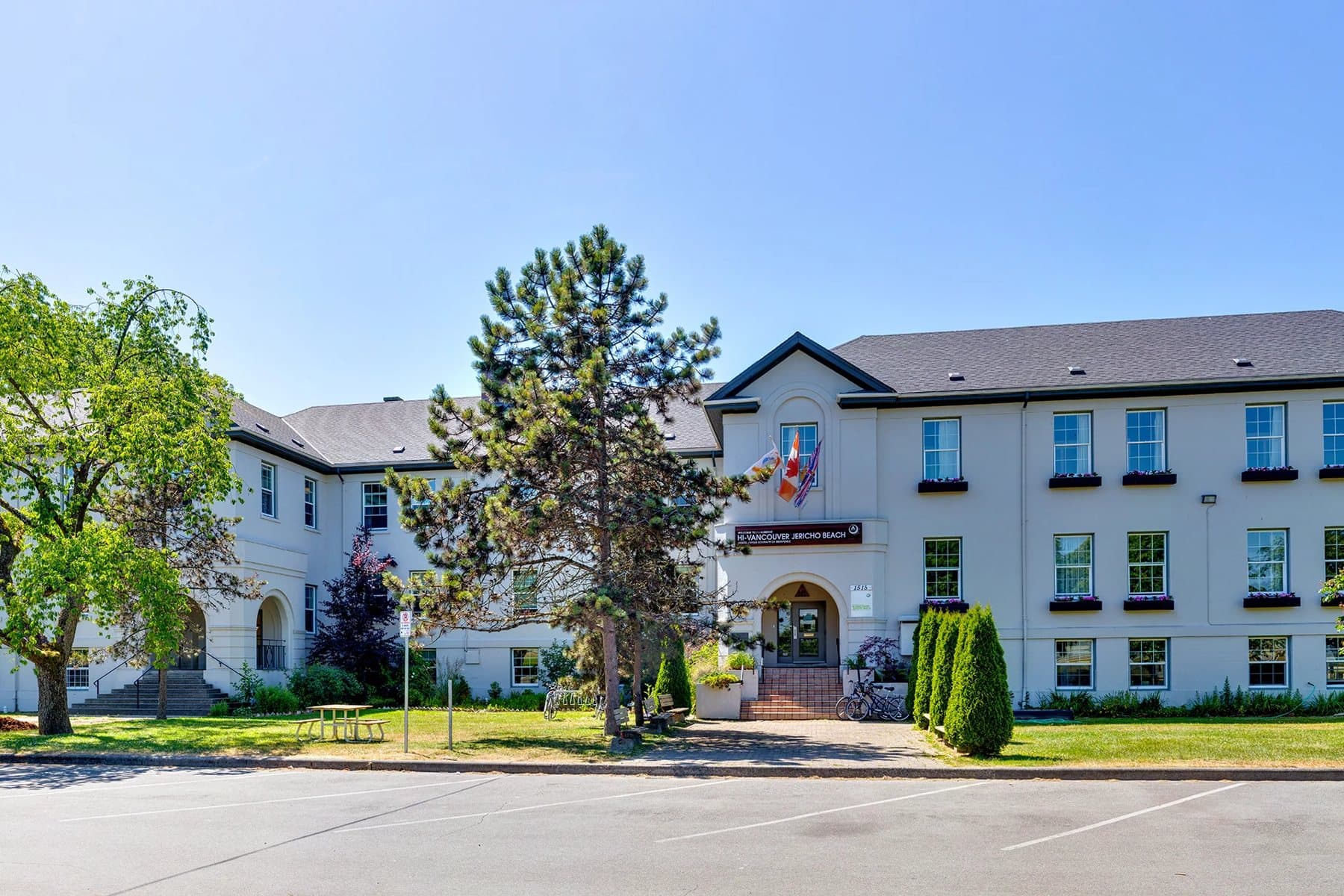 The white main building of HI Vancouver Jericho Beach hostel under a clear blue sky.