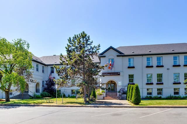 The white main building of HI Vancouver Jericho Beach hostel under a clear blue sky.