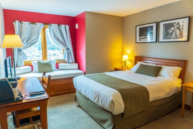 Guest room at Howe Sound Inn with a queen bed, window seat and red accent wall.