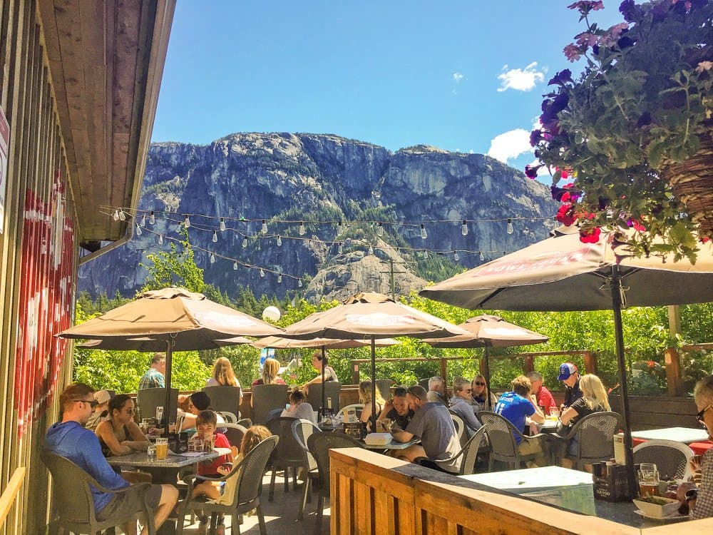 Diners under umbrellas on the Howe Sound Inn patio with the Stawamus Chief rising behind.