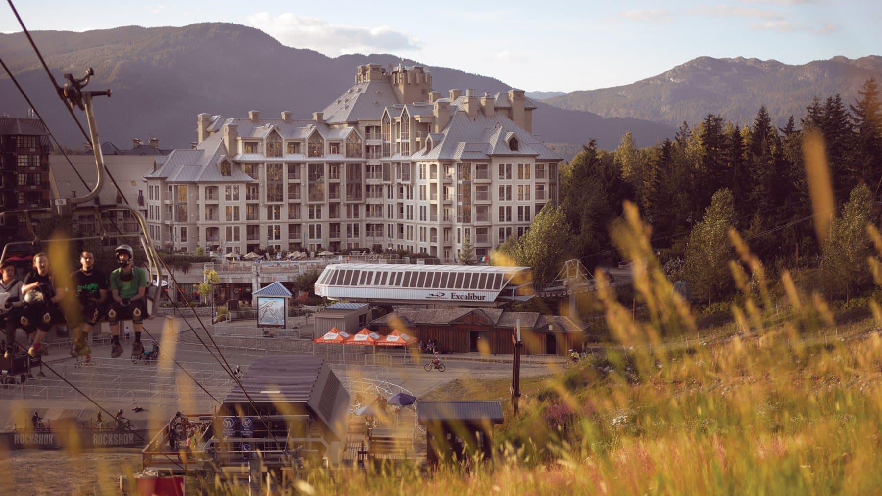 Pan Pacific Whistler Mountainside seen over summer grass with a gondola cabin in the foreground.
