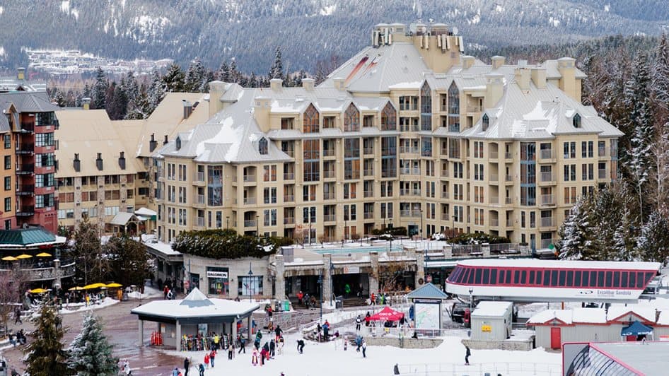 Pan Pacific Whistler Mountainside hotel above Whistler Village with snow on the roofs and the slopes behind.