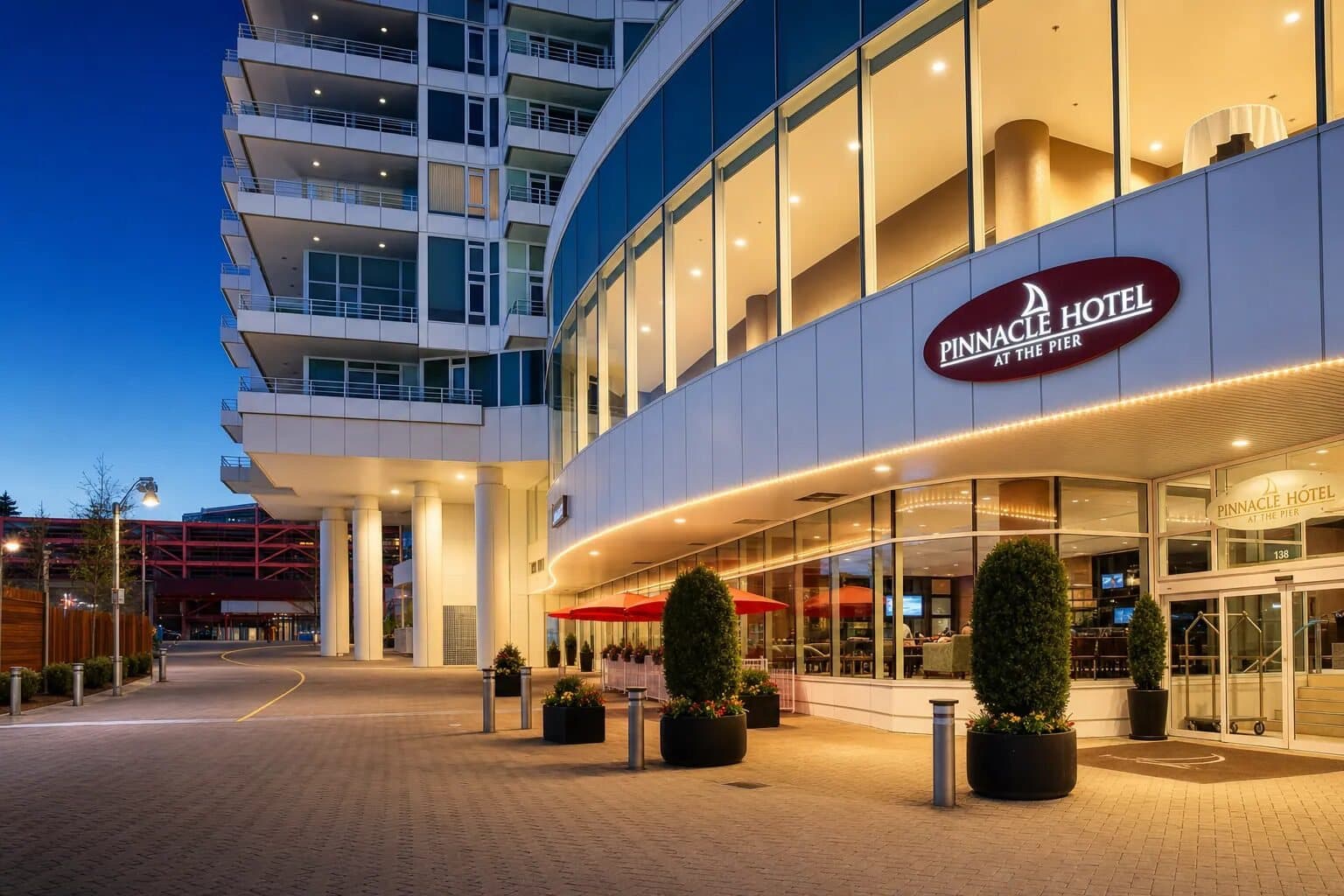 Curved glass entrance and tower of Pinnacle Hotel at the Pier lit up at dusk.
