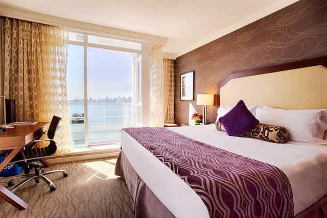 Guest room at Pinnacle Hotel at the Pier with a king bed and a wall of windows facing the water.