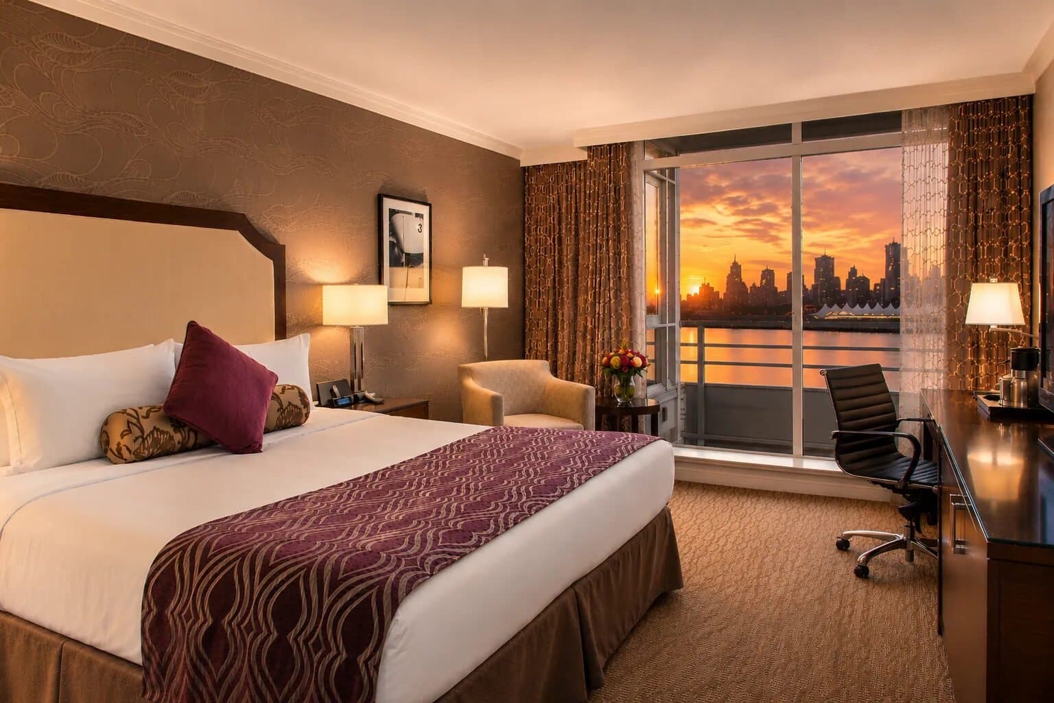 Guest room at Pinnacle Hotel at the Pier with a balcony looking onto a sunset over the harbour.