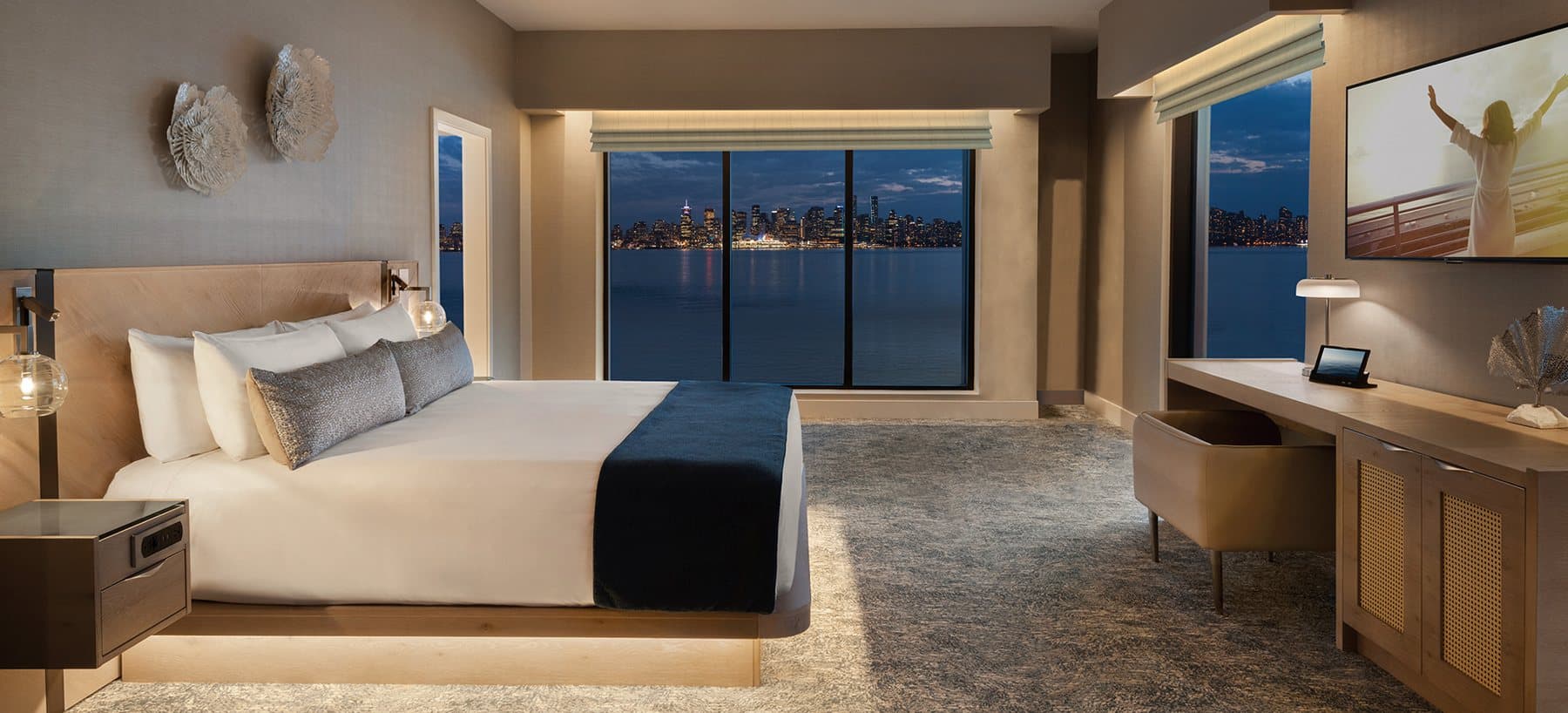 Suite at Seaside Hotel with a king bed and a window wall facing the harbour and the city skyline.