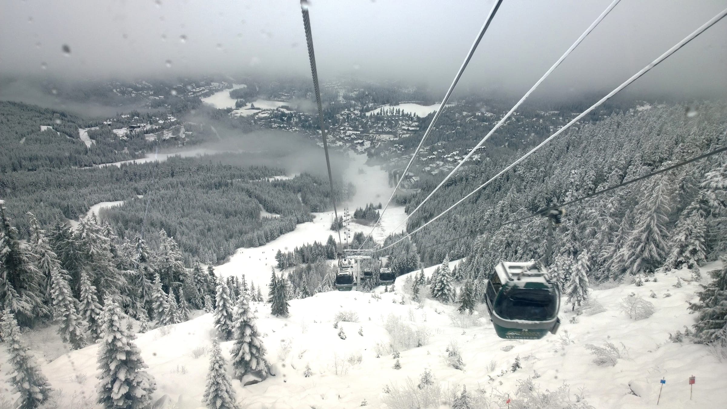 The Creekside Gondola climbs over snow-loaded forest above Whistler Creekside on a grey December day.