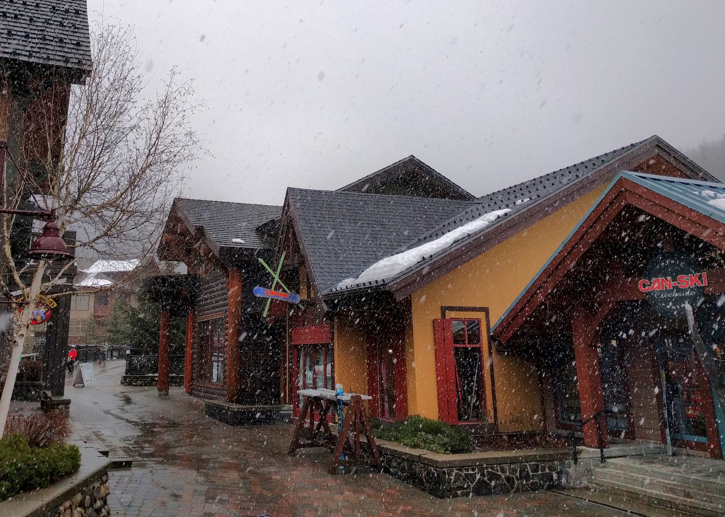 Snow falls past the timber shopfronts and wet paving stones of Whistler Creekside in February.