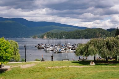 People stroll the lawn of Deep Cove's waterfront park beside the marina under a cloudy summer sky. (Deep Cove)