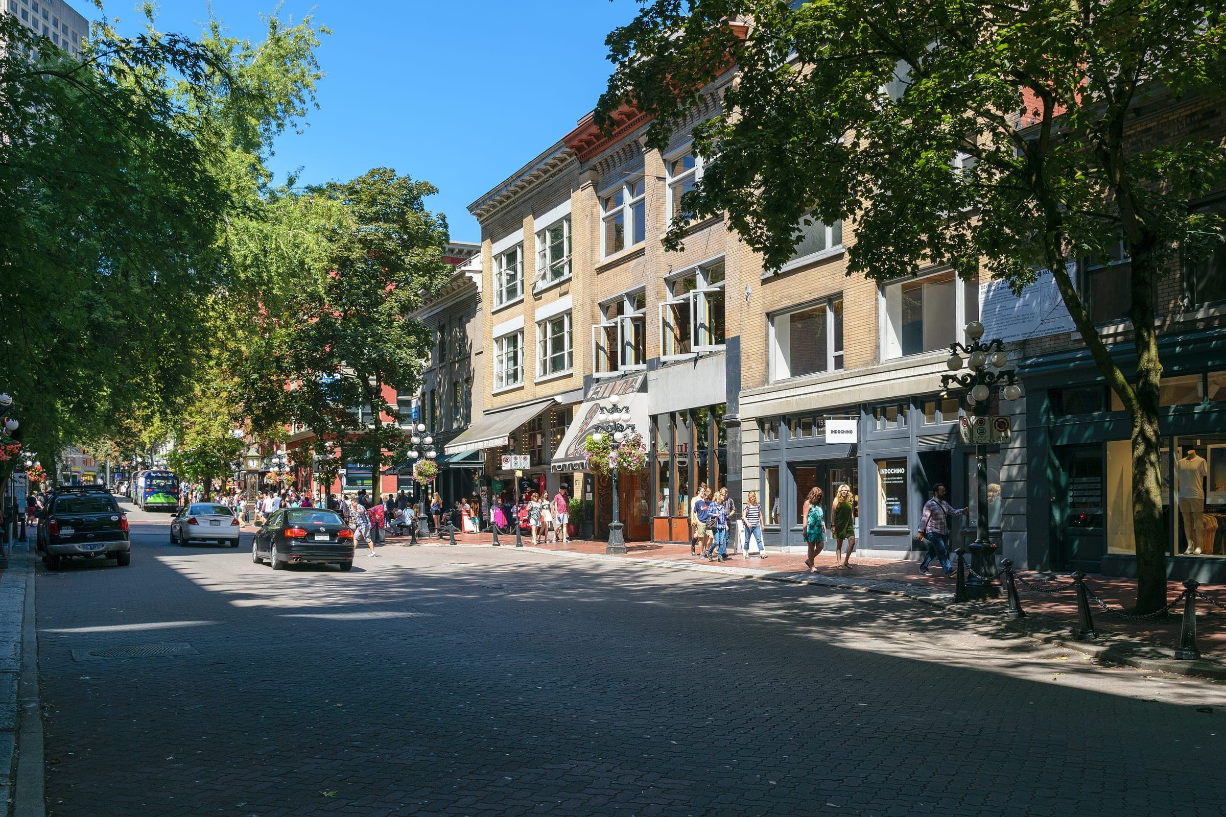 Shoppers stroll the brick sidewalks of Water Street in Gastown under the shade of summer trees.