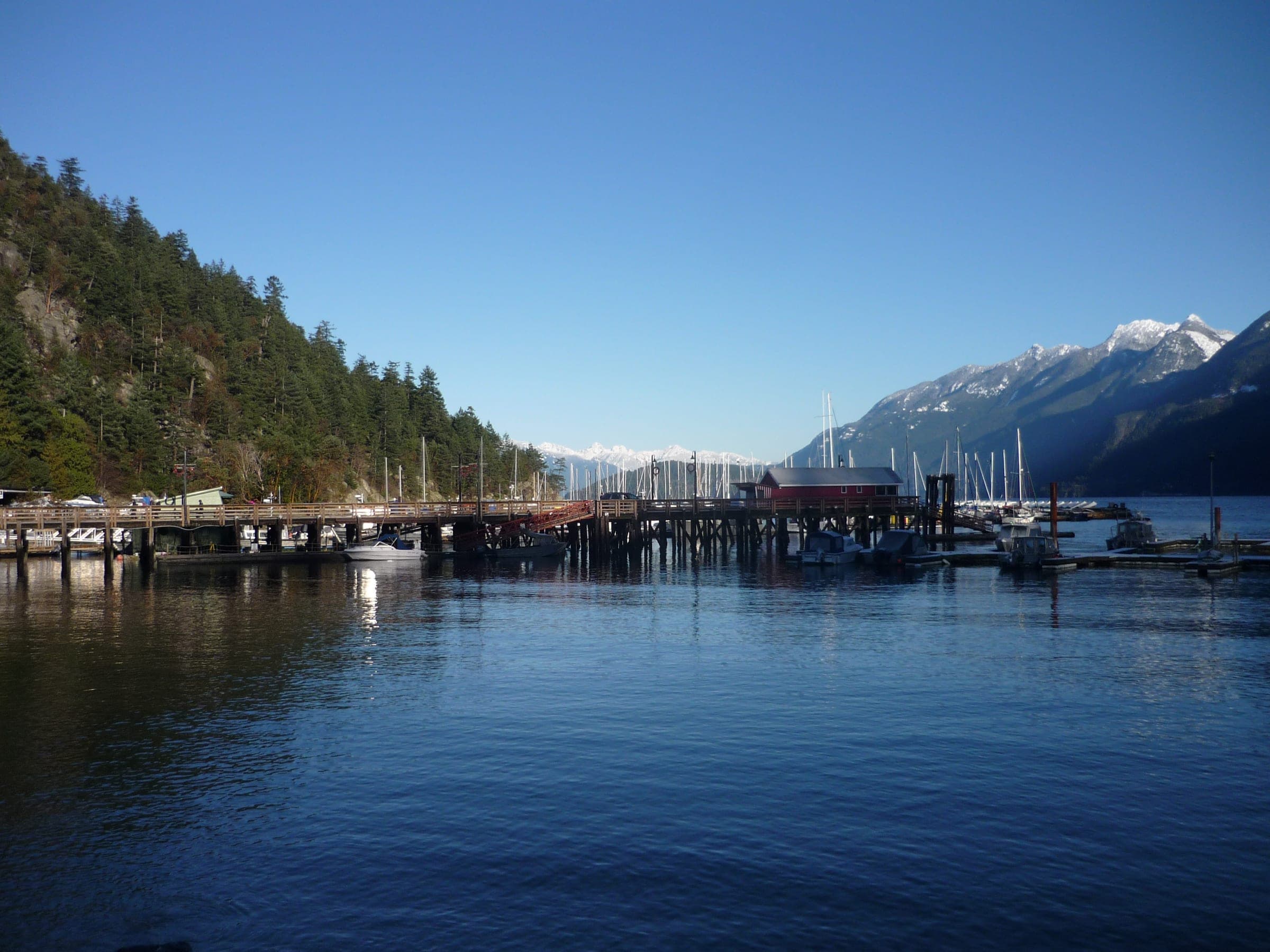 The Horseshoe Bay wharf stretches across still blue water below the snowy peaks of Howe Sound in December.