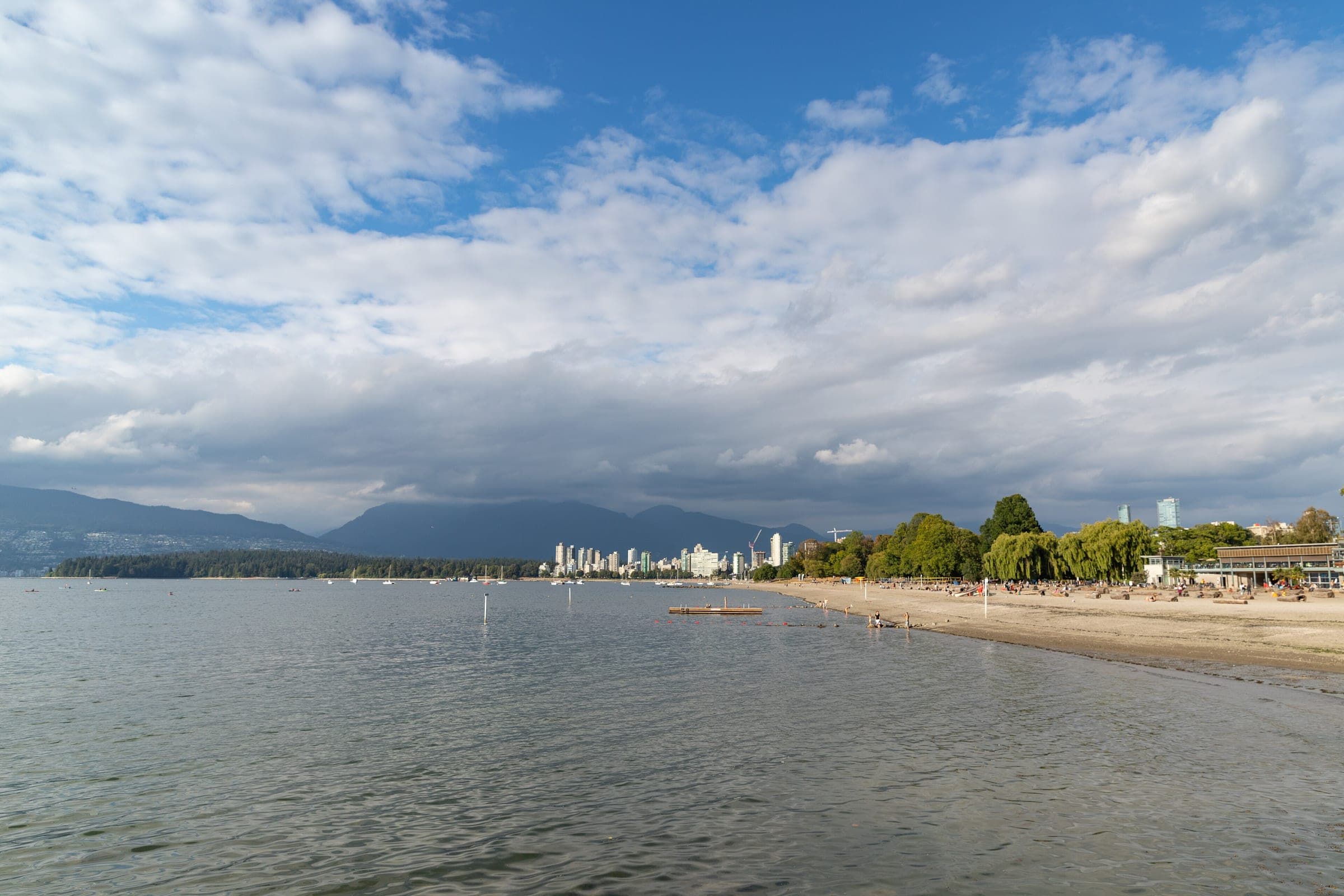 Big clouds roll over English Bay as the sand of Kitsilano Beach curves toward the downtown towers.