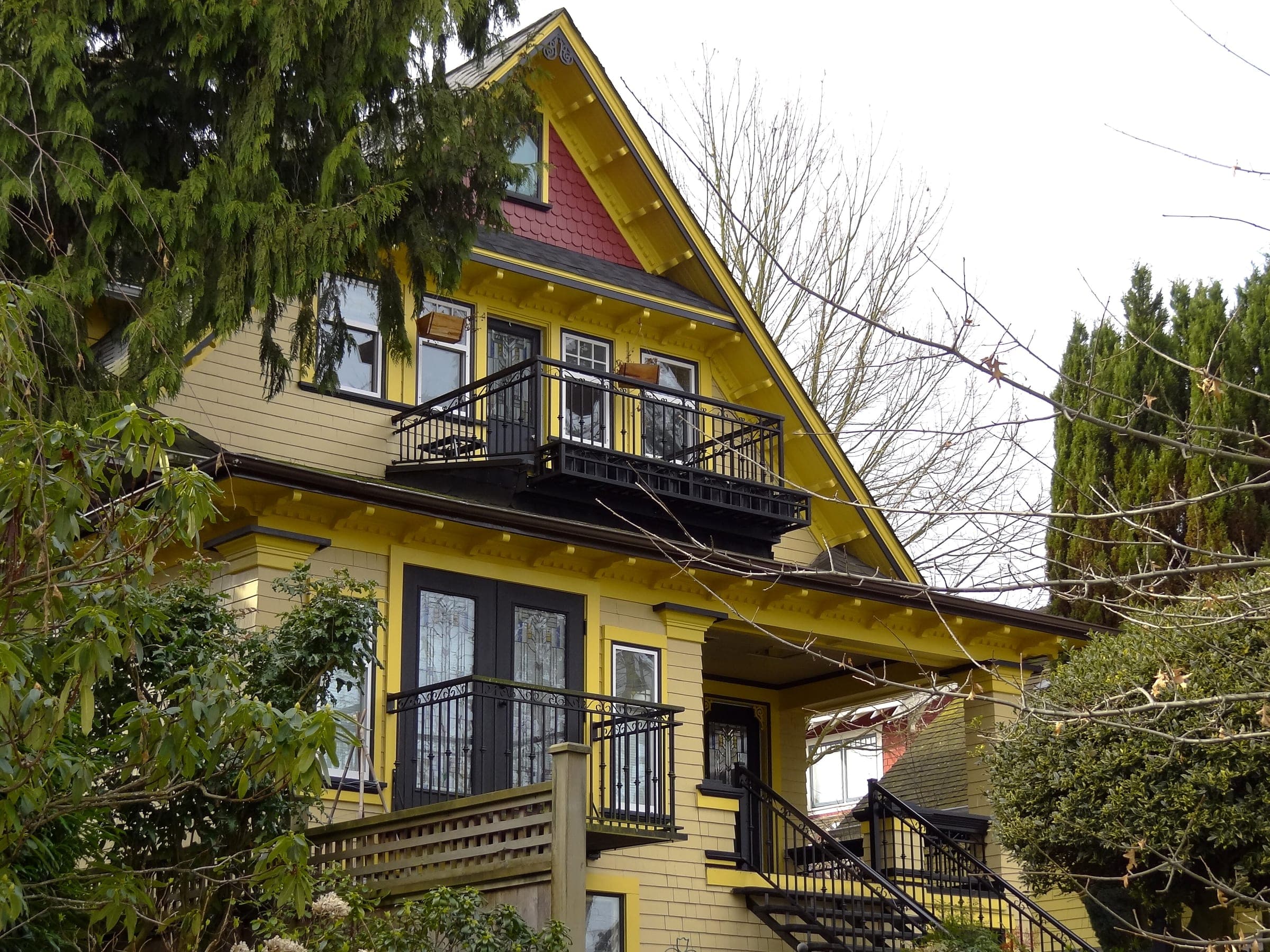 A yellow heritage house with stacked balconies and a red gable stands among trees in Mount Pleasant.