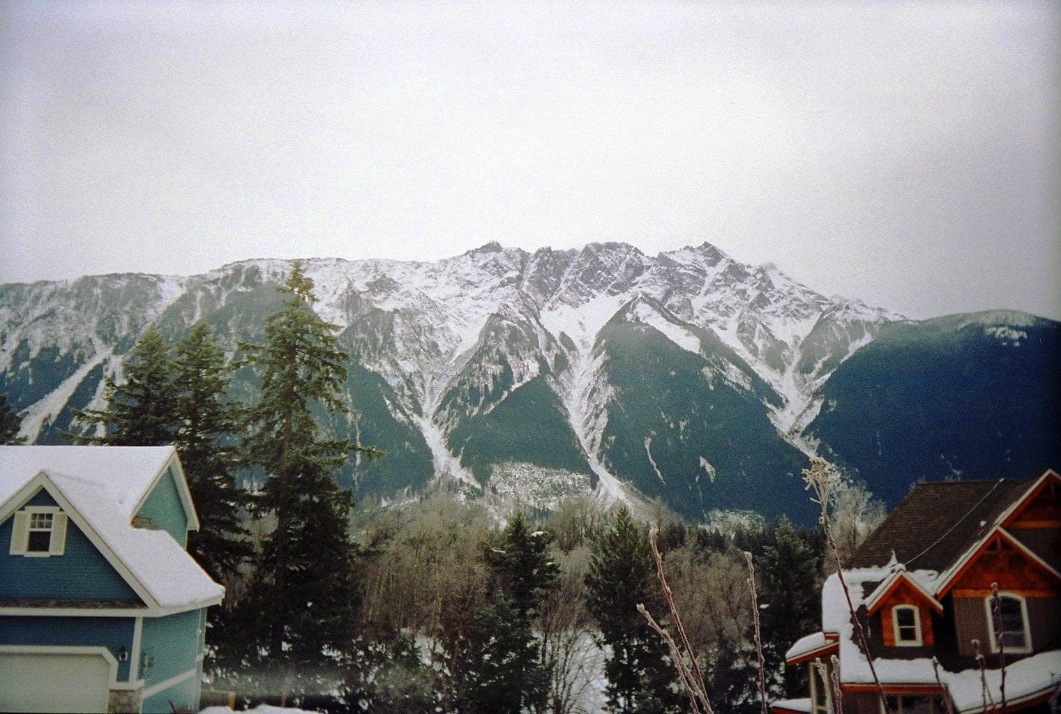 Snow streaks the face of Mount Currie above the snow-covered rooftops of Pemberton on a grey winter day.