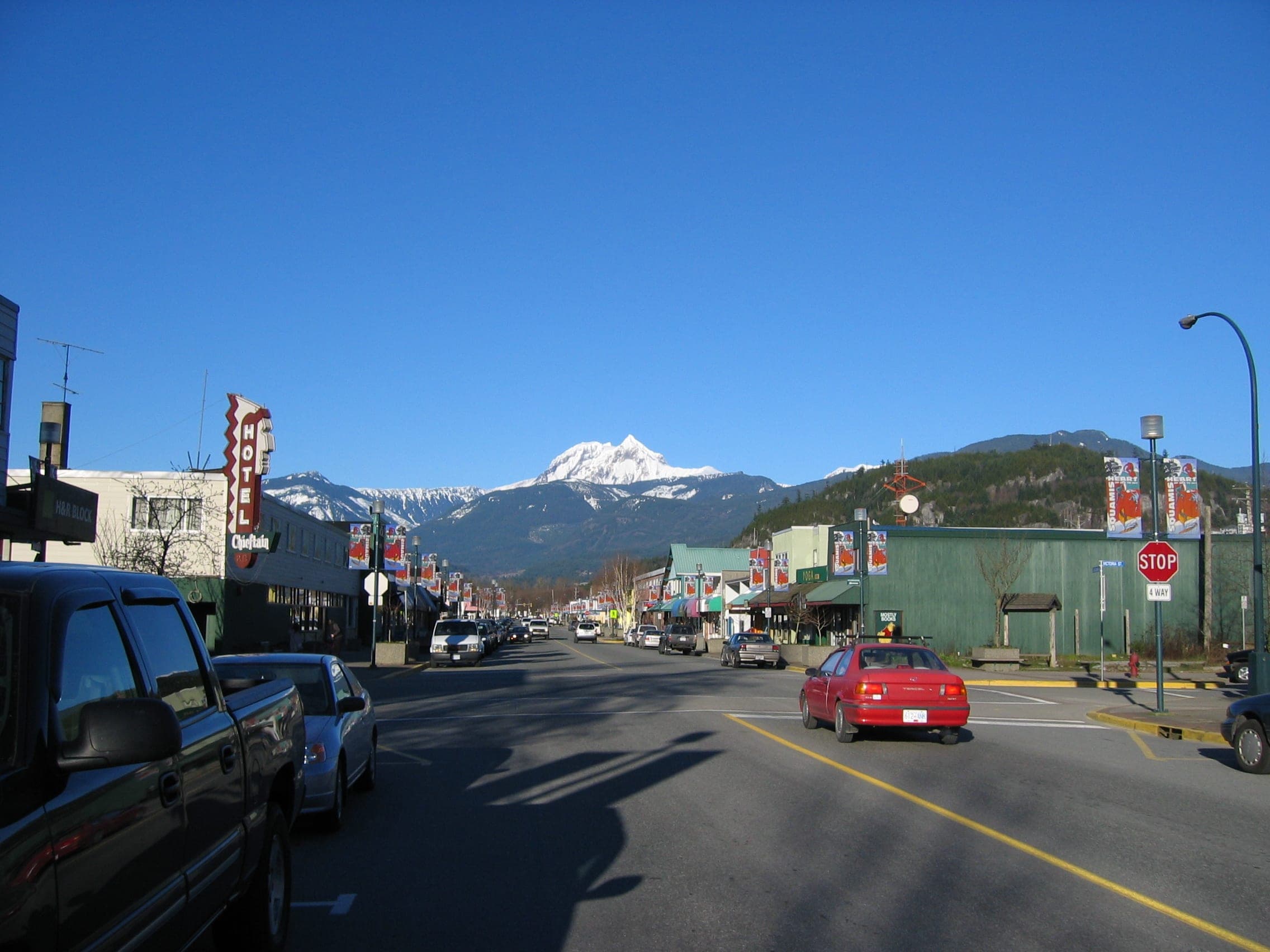 Cleveland Avenue runs through downtown Squamish toward a snow-covered peak under a clear blue sky.