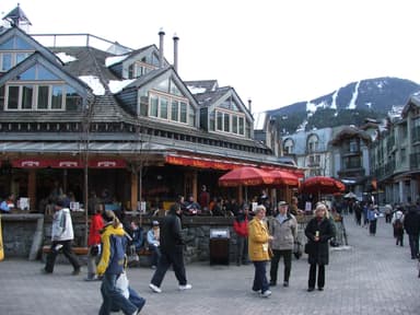 Skiers and walkers pass a busy patio on the Whistler Village Stroll below the snowy runs of Whistler Mountain. (Whistler Village)