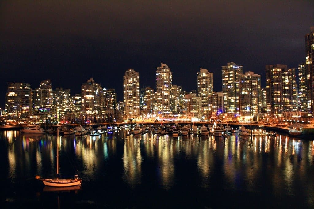 Yaletown's towers and the marina lights shine on the still water of False Creek at night.