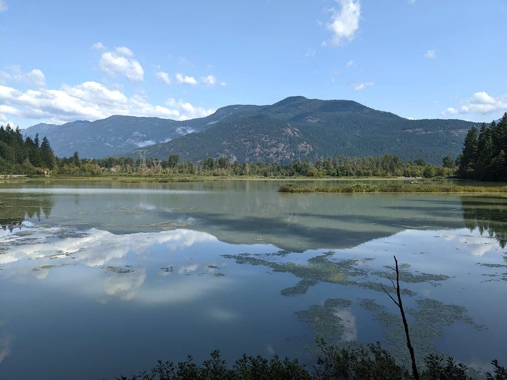Clouds and the wooded ridge above Pemberton lie doubled in the calm water of One Mile Lake.
