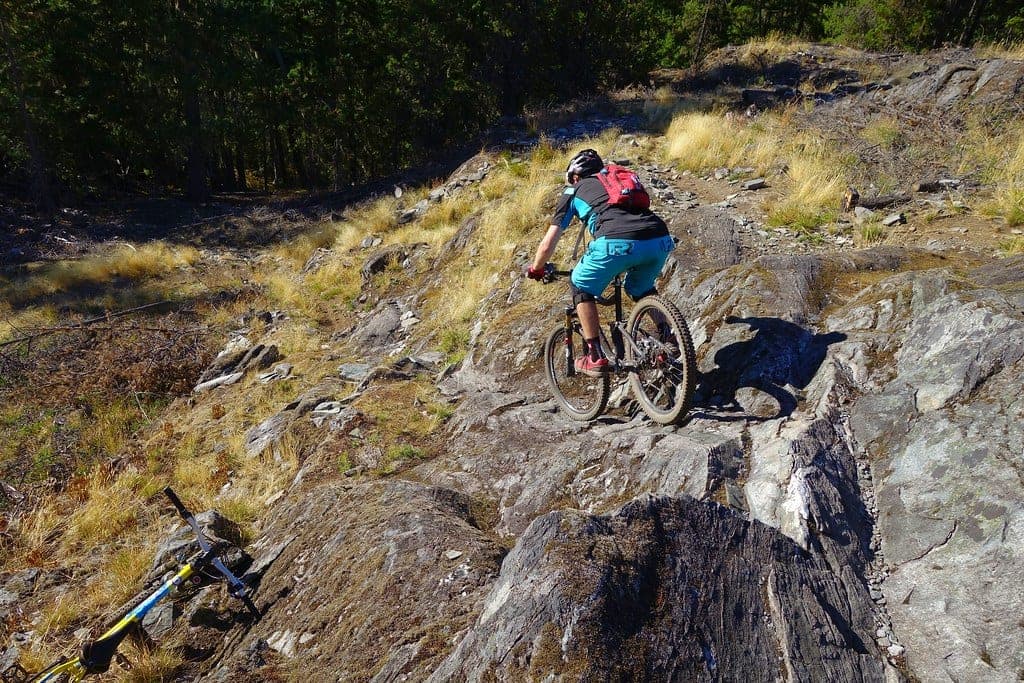A rider picks a line down rough rock among dry grass on the One Mile Lake side of Pemberton's trails.