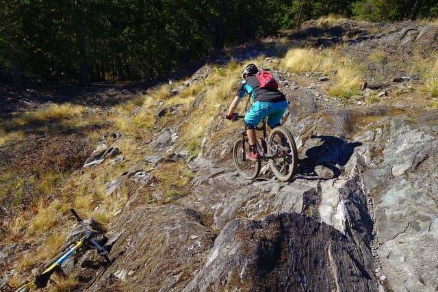 A rider picks a line down rough rock among dry grass on the One Mile Lake side of Pemberton's trails.