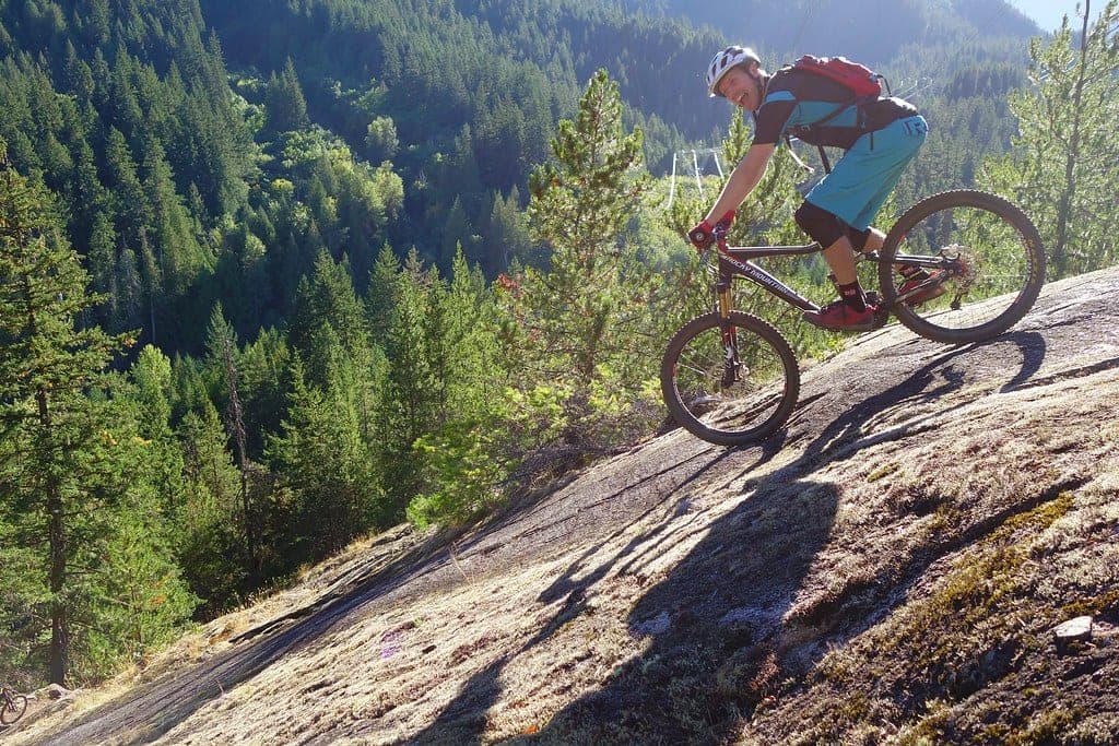 A rider leans down a steep granite slab on Tower of Power above One Mile Lake in Pemberton.