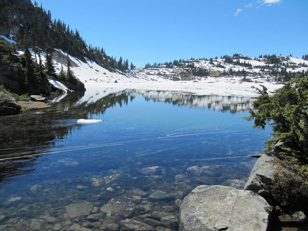 Clear water at Rainbow Lake mirrors the snowy alpine ridges above Whistler in early summer.