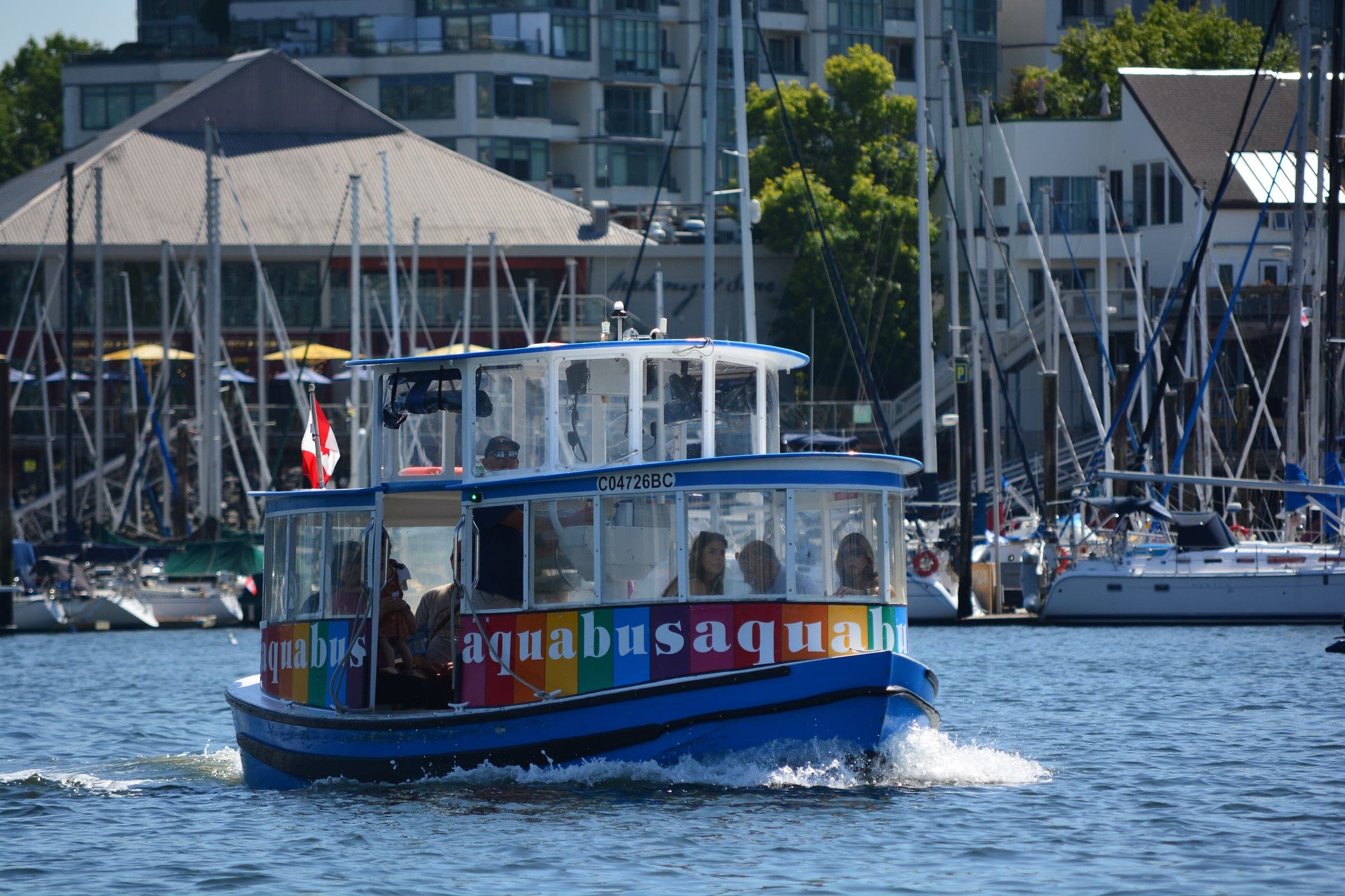 A blue Aquabus ferry crosses False Creek with the Vancouver marina and towers behind it.